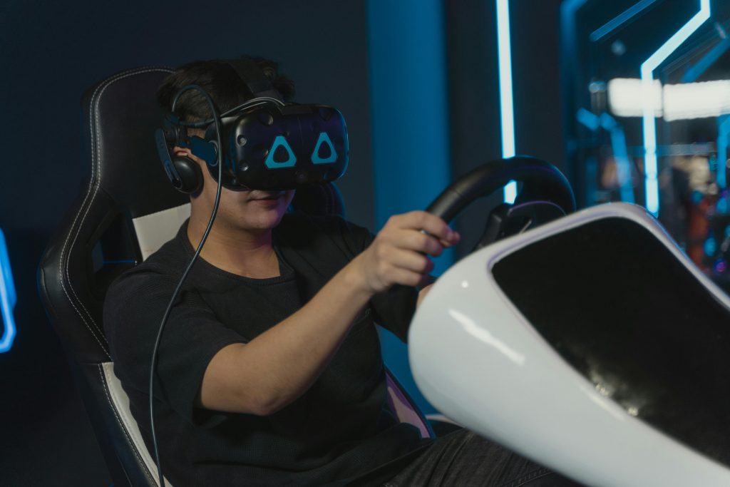 Man engaging in immersive virtual gaming with VR headset and steering wheel setup indoors.